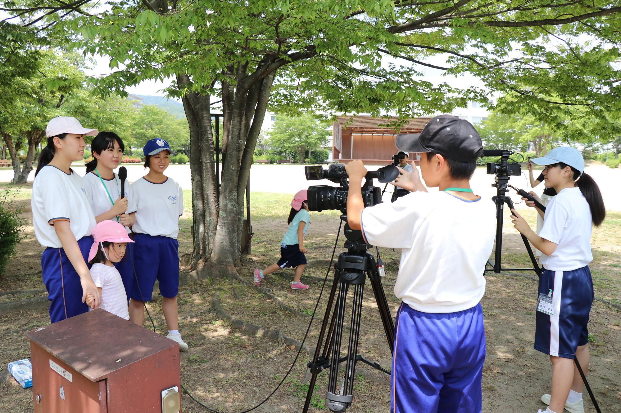 夢公園内にて園児にインタビューする生徒とそのインタビューをビデオ撮影する生徒の写真
