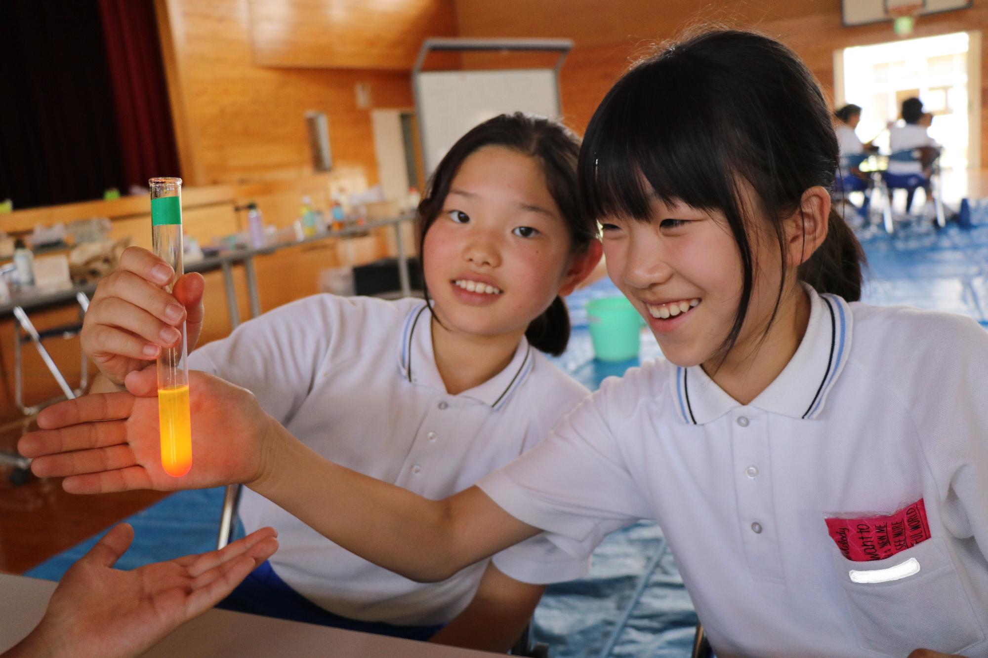 ケミカルライトの原理を実験する児童らが試験官の中の液体が光る現象を楽しんでいる写真