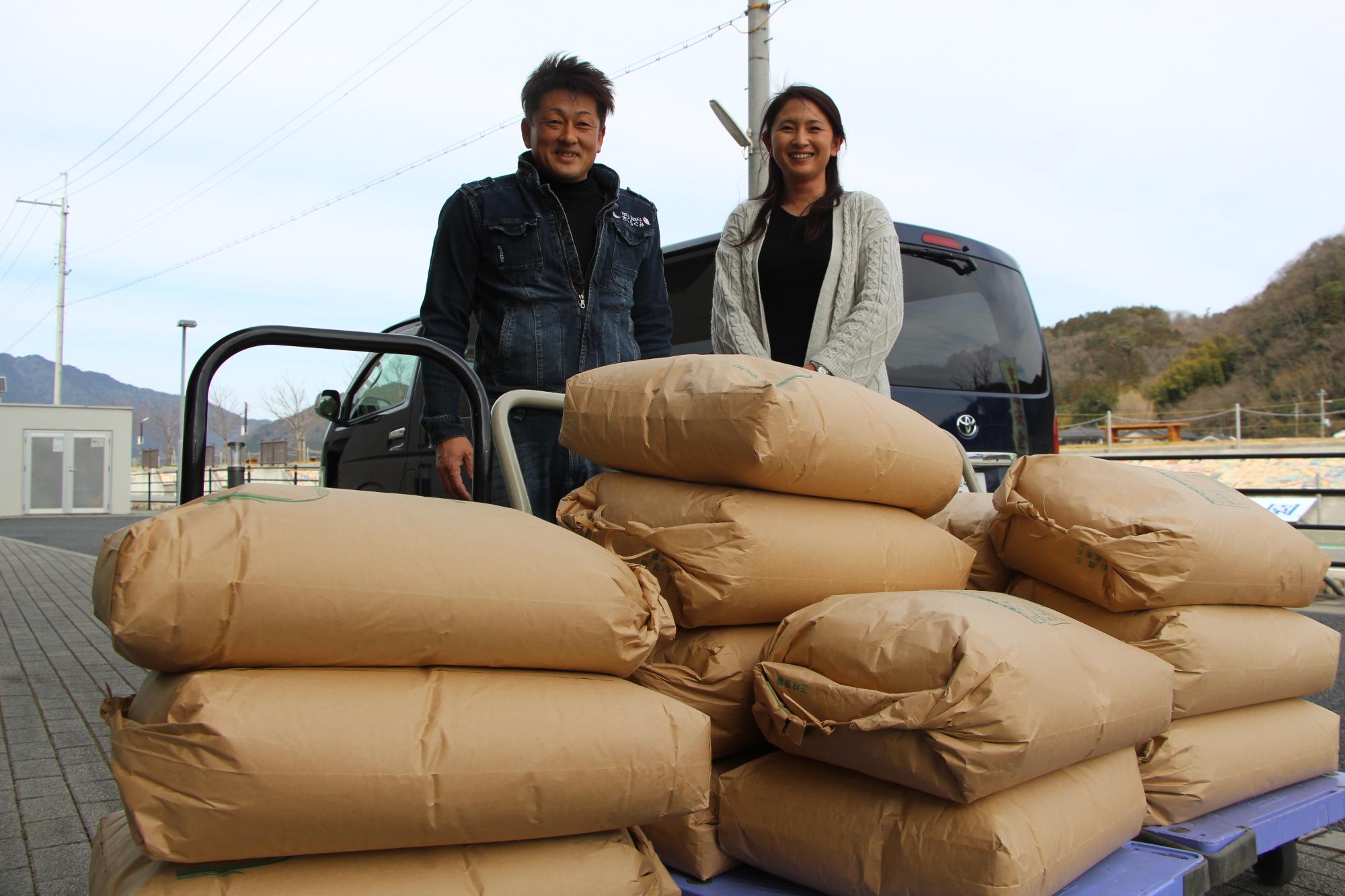 山崎町の久宗さんが米15袋を市に寄贈し、積み上げられた米袋のうしろで笑って立っている写真
