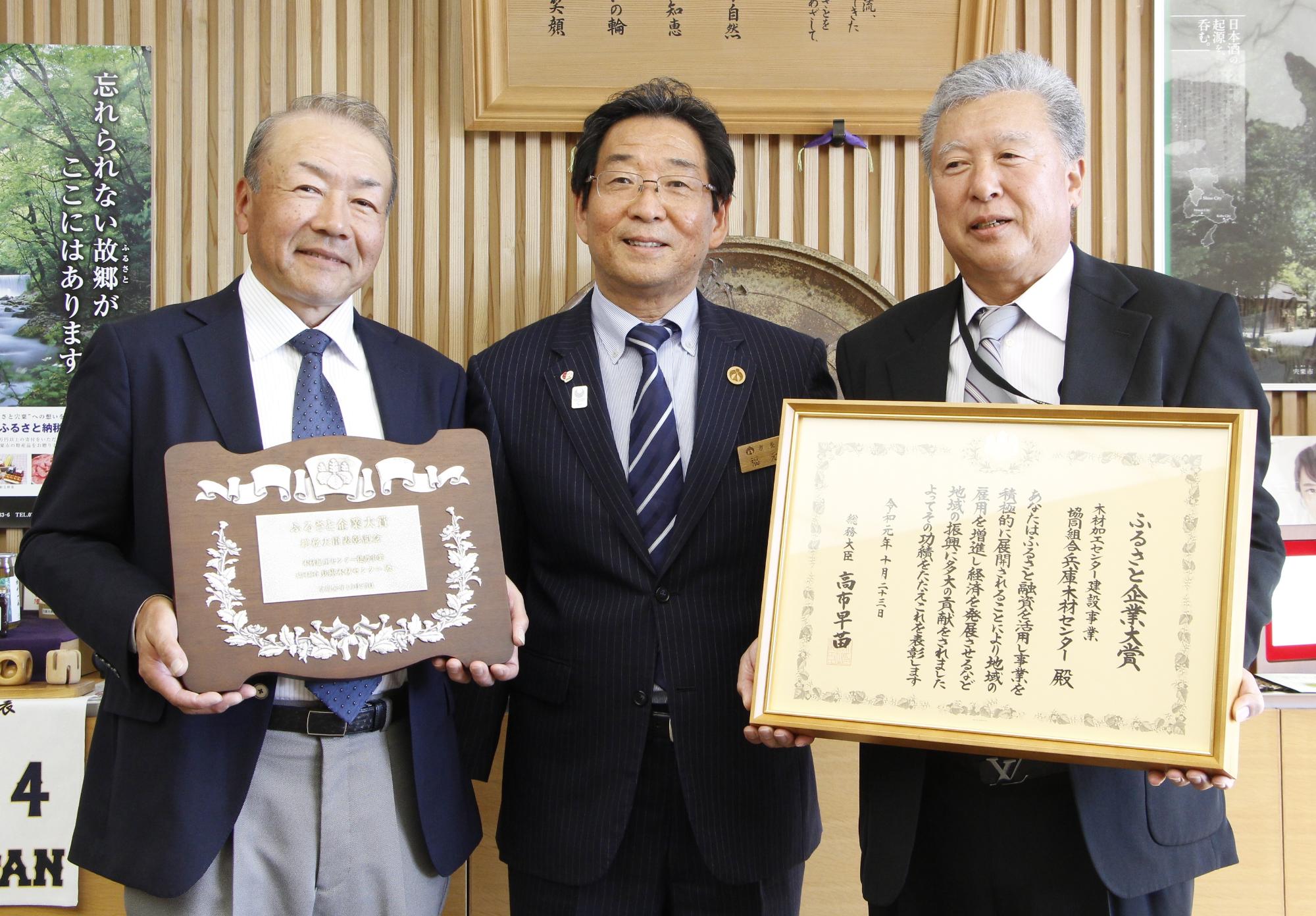 表彰状を持ったひょうご木材センターの役員二人と市長が並んで笑っている写真