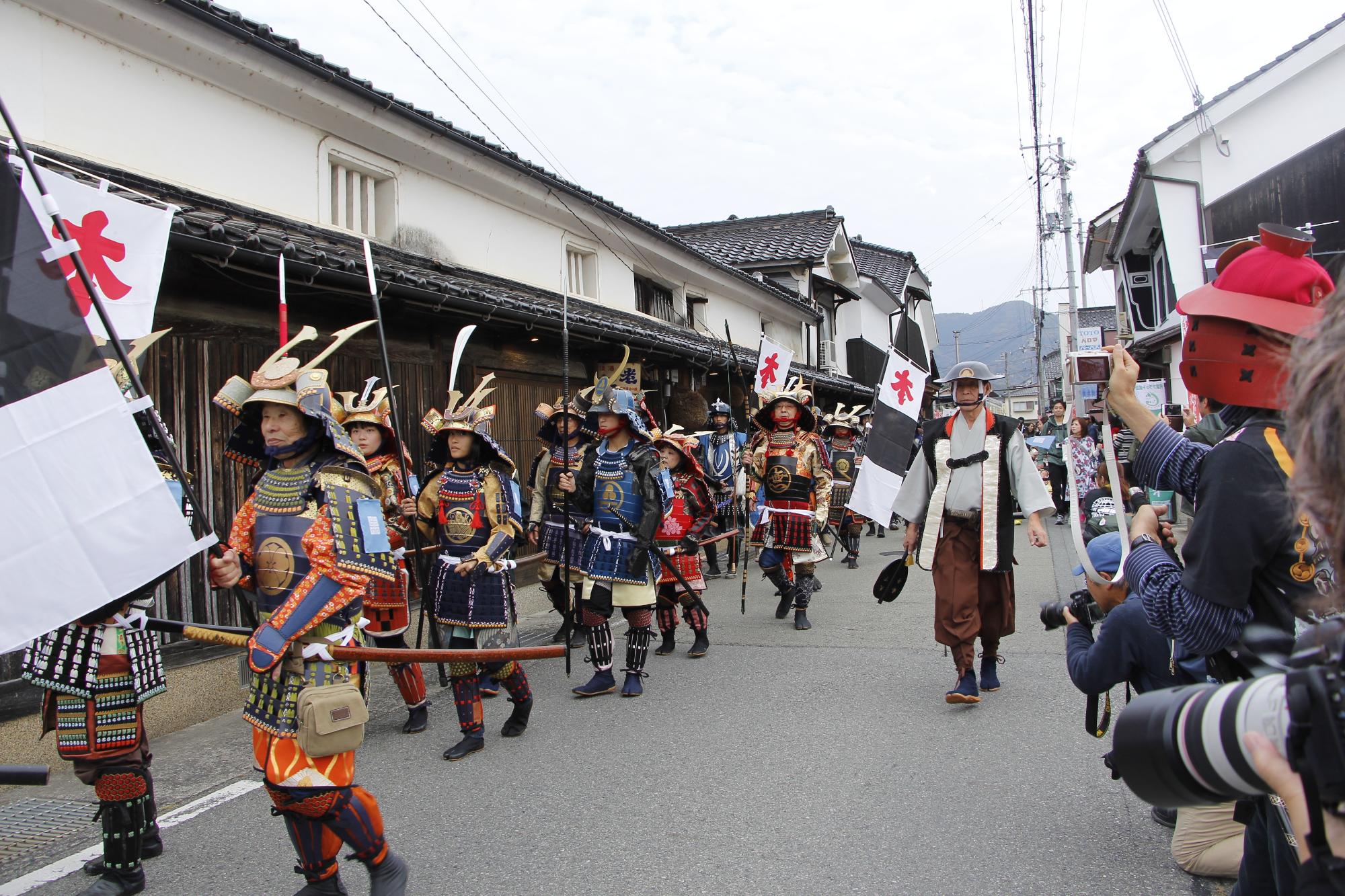 山崎町鹿沢の酒蔵通りを練り歩く武者行列に写真愛好家らがカメラを向けている写真