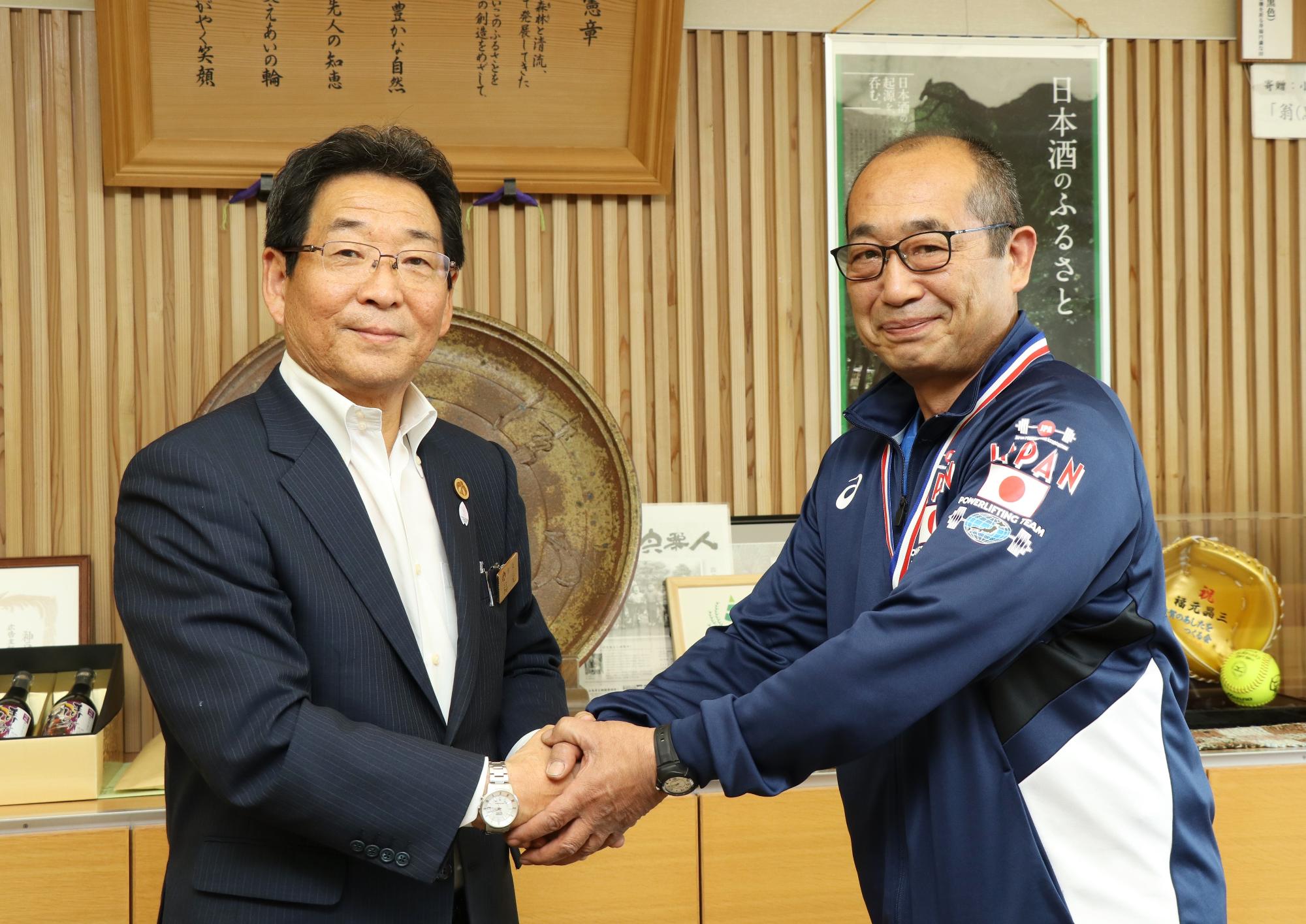 紺のジャージを着たの伊藤さんが市長と握手をしている写真