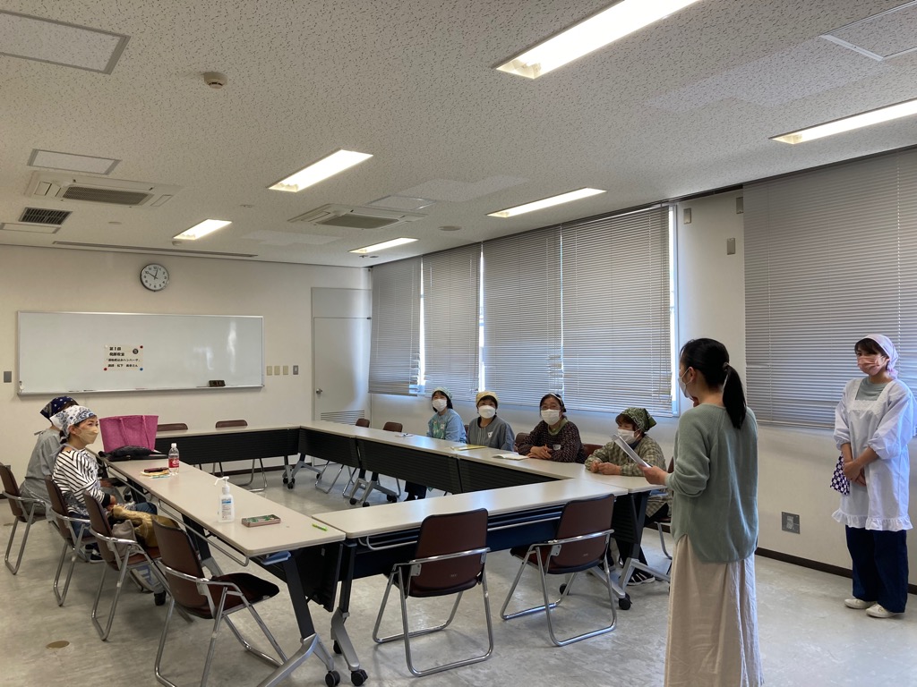 会議テーブルを囲んで参加者がいすに座り、講師の話を聞いている写真