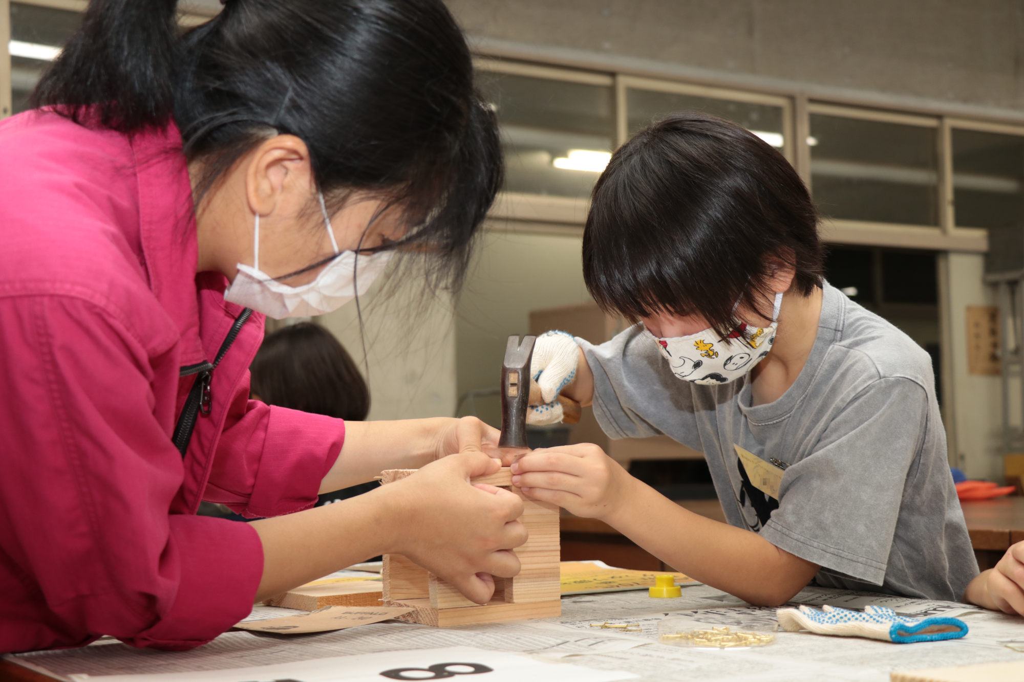 山崎高校の生徒から手ほどきを受けながら釘を打つ女子児童の写真