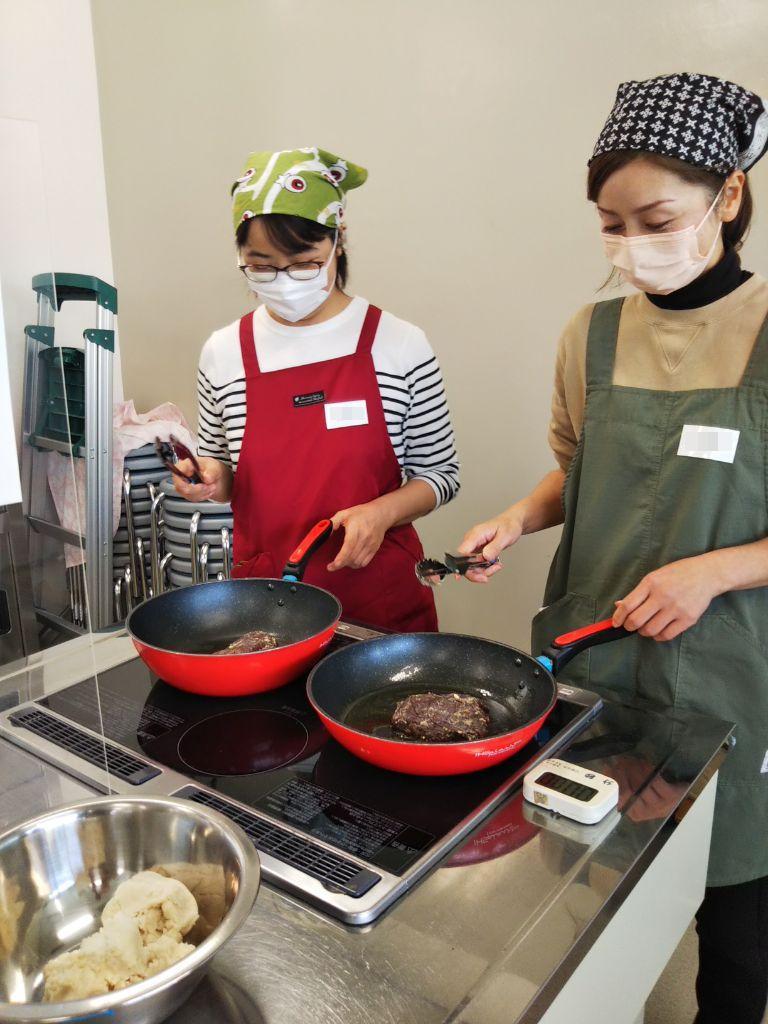 参加者がフライパンをつかって鹿肉の塊に火を通している写真