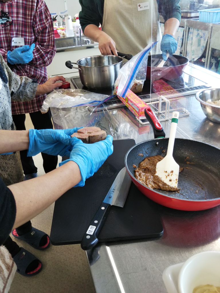 酒粕入りのソースをつくっている横で参加者が鹿肉の断面をみて火の通り具合を確かめている写真