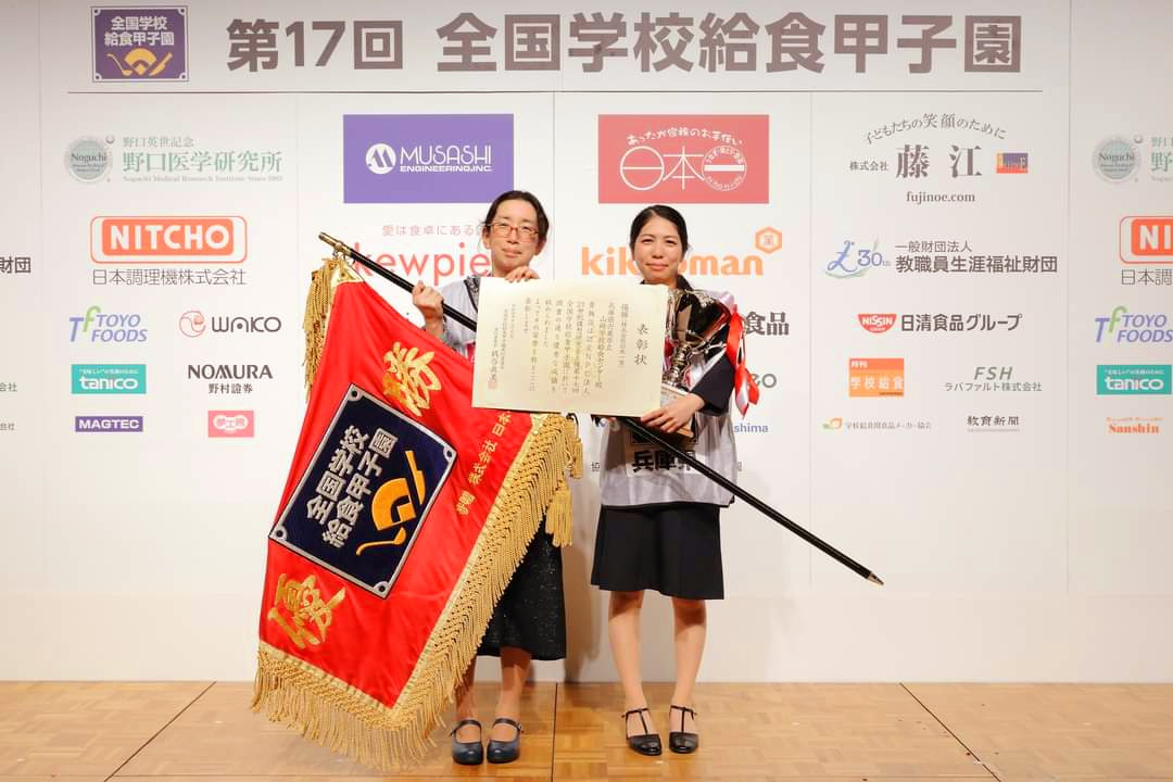 第17回全国学校給食甲子園で優勝の賞状と優勝旗を手に微笑む世良栄養教諭と安原調理師の写真