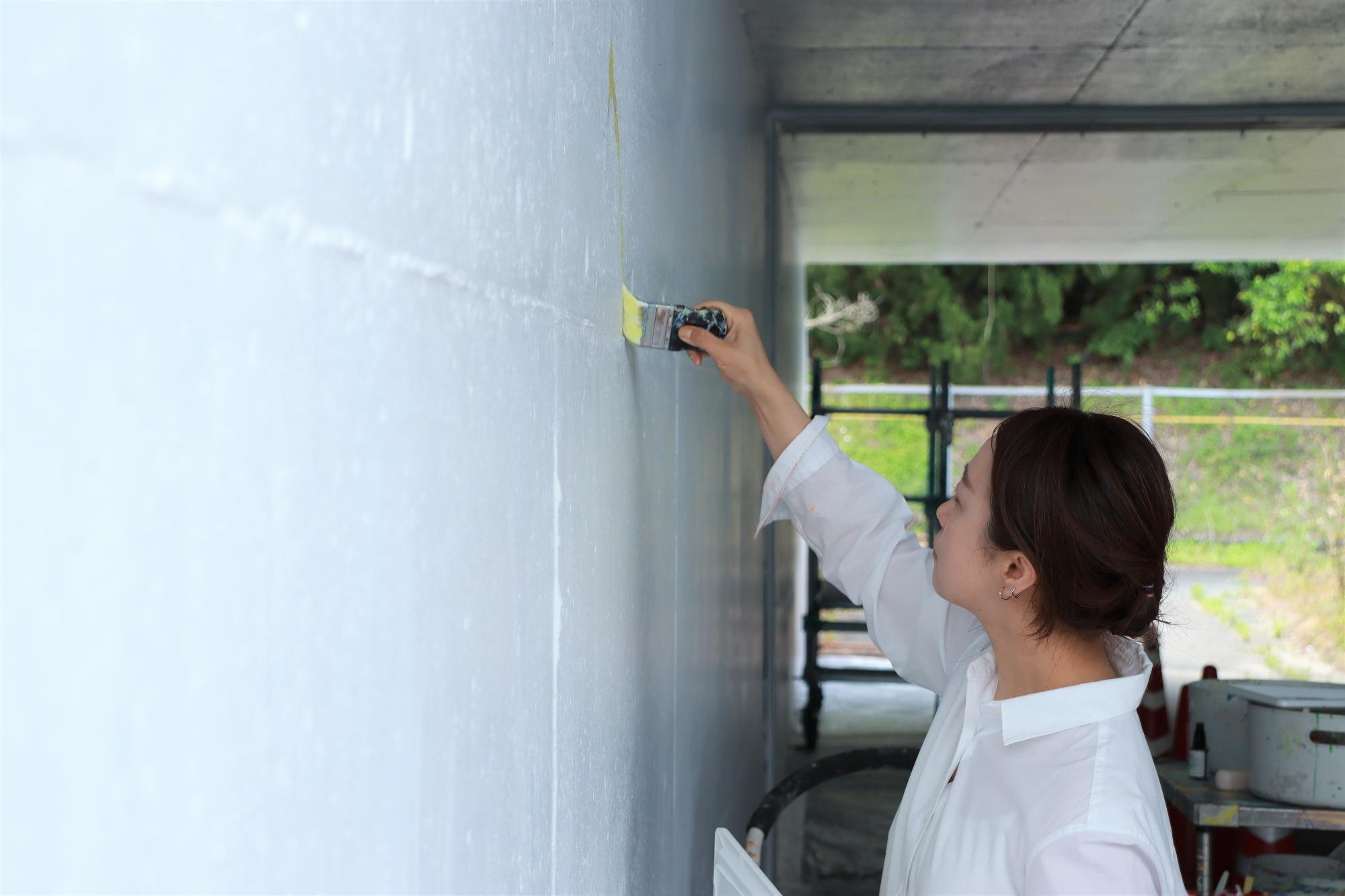 美術作家の植田志保さんがハケで通路壁面へ色を塗り始めた写真
