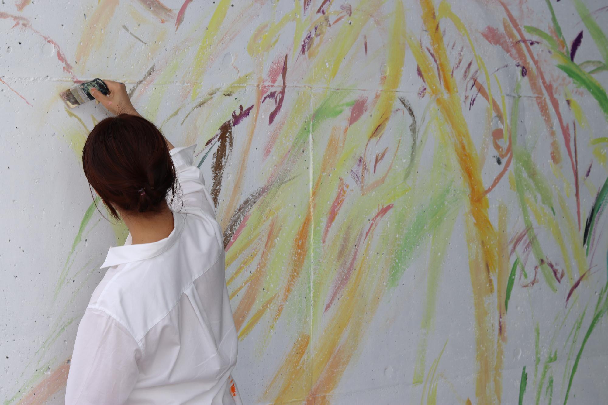 美術作家の植田志保さんが多彩な色で通路壁面に壁画を描いている写真