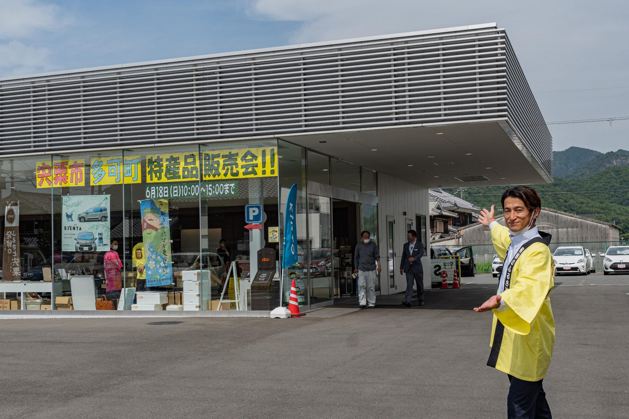 地域おこし協力隊の松下さんがトヨペット西脇店の外で販売会の看板をPRしている写真
