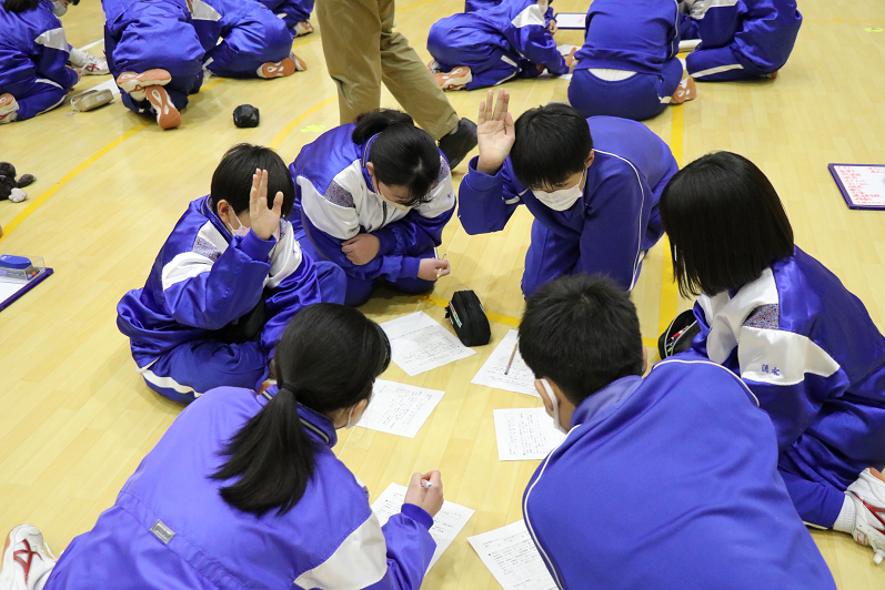 生徒たちが体育館で円になって座り、防災バッグの中身について話し合っている写真