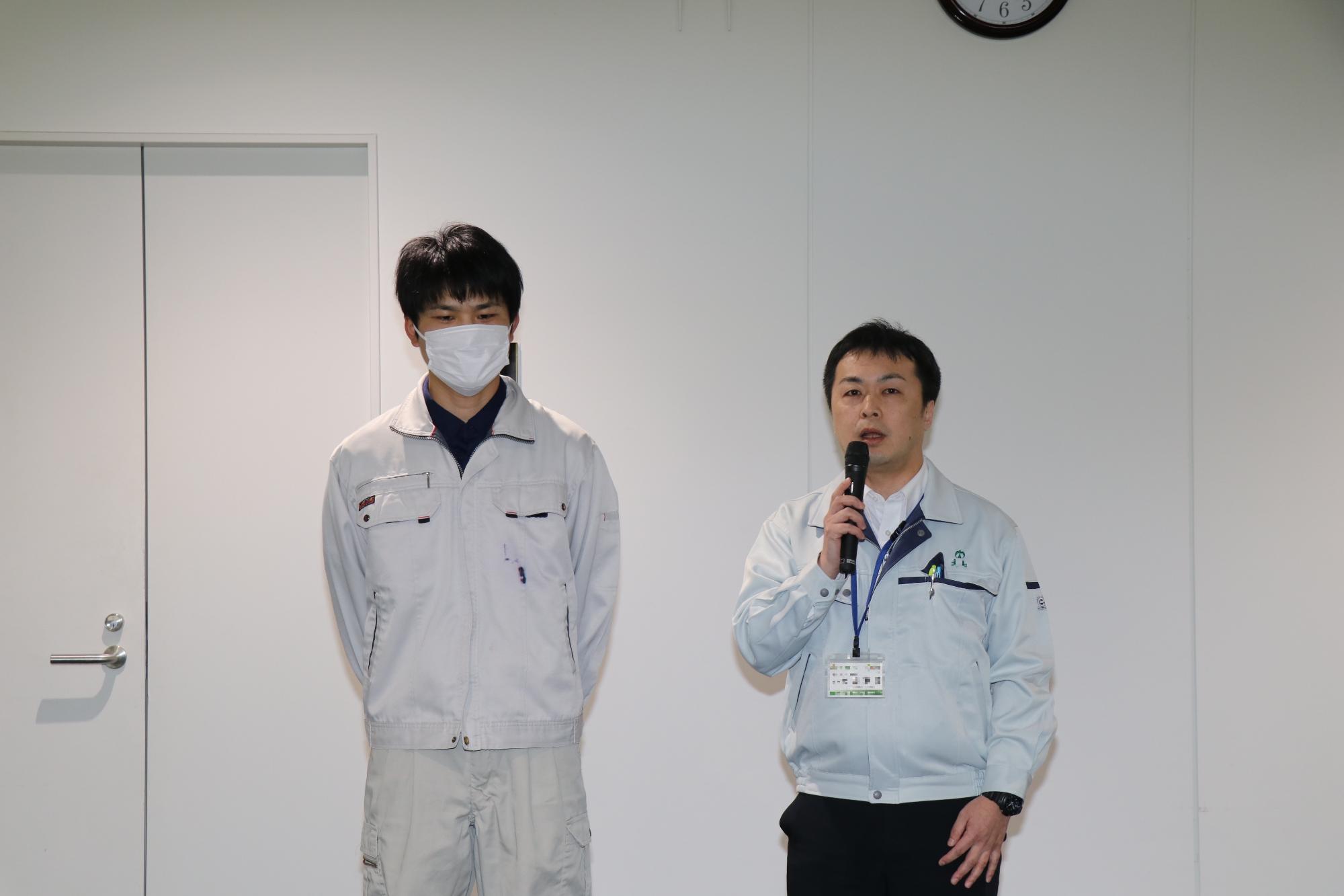 市役所3階ロビーで派遣される職員二人が横に並び、1人がマイクを持って決意表明をしている写真