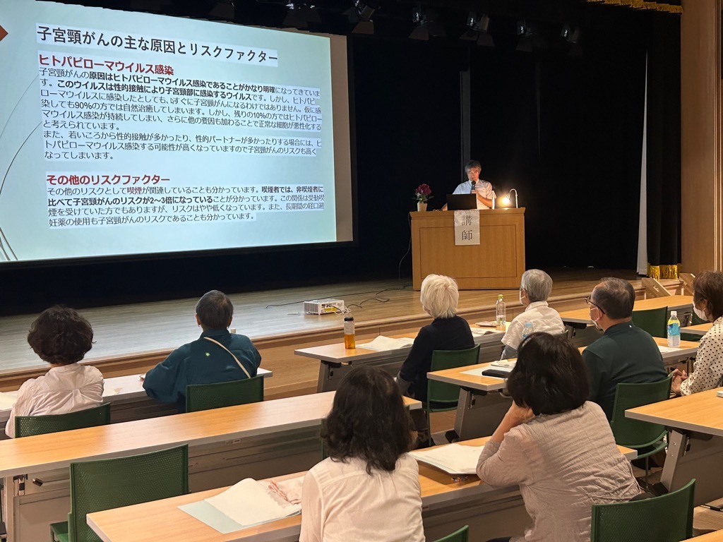 講座の受講生が聴講する中、子宮頸がんの原因についてスライドを使って講師が説明している写真