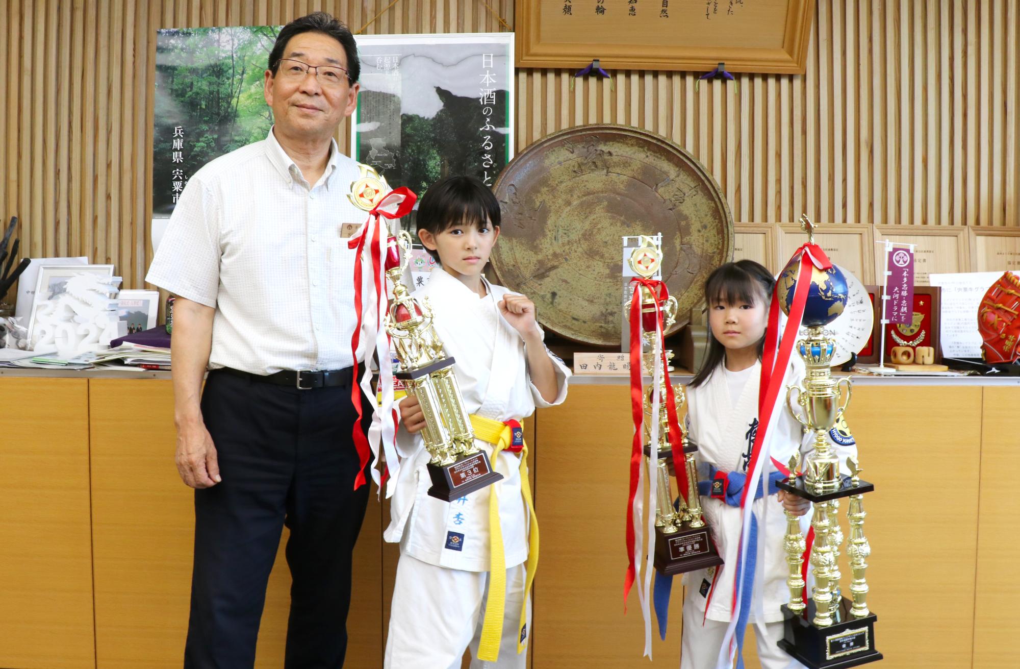 大会トロフィーを手に持った小林さん(右)と坂井さん(中央)が福元市長と並んでいる写真