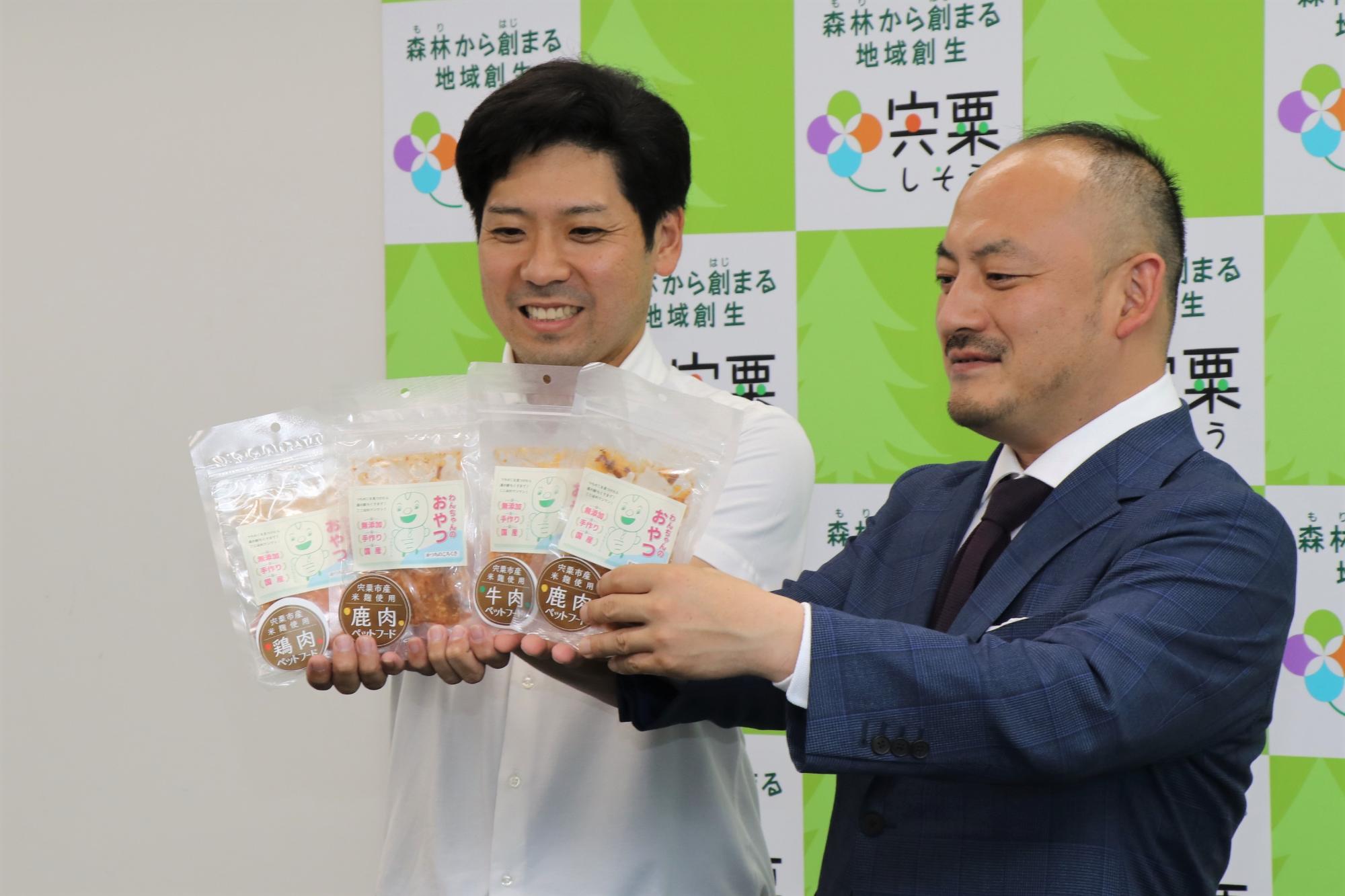 道の駅ちくさの運営事業者の代表者2人が開発した犬用の発酵食「わんちゃんのおやつ」を手にもって正面に掲げている写真