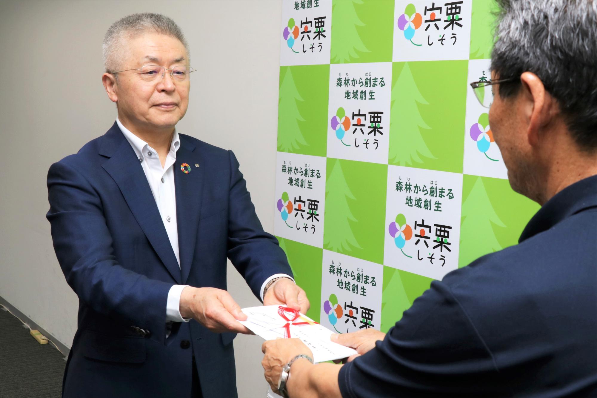 西兵庫信用金庫の桑垣理事長が図書券贈呈式で目録を福元市長に手渡している写真