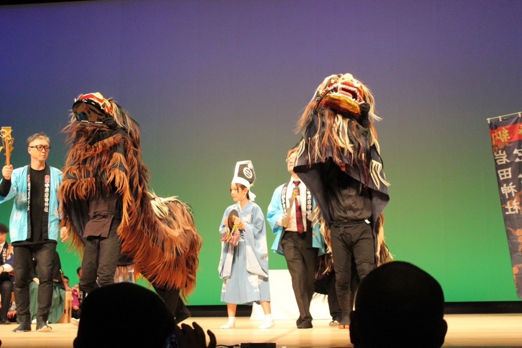 舞台上で演じている2体の獅子舞の頭の部分を大きく持ち上げているところの写真