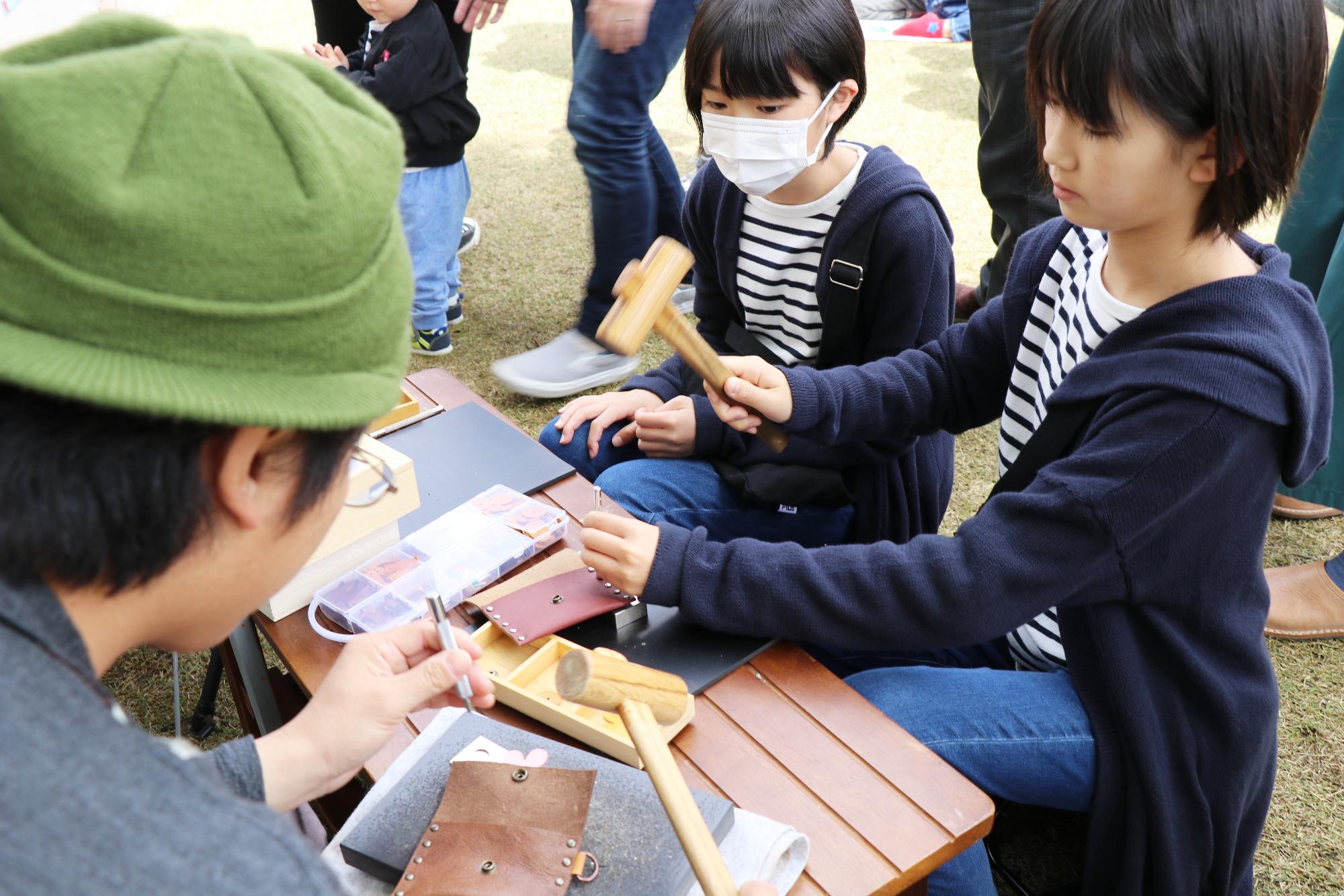 おそろいの紺色のパーカーとボーダーのTシャツを着た二人の子どもが木槌を使い革製品を作っている写真
