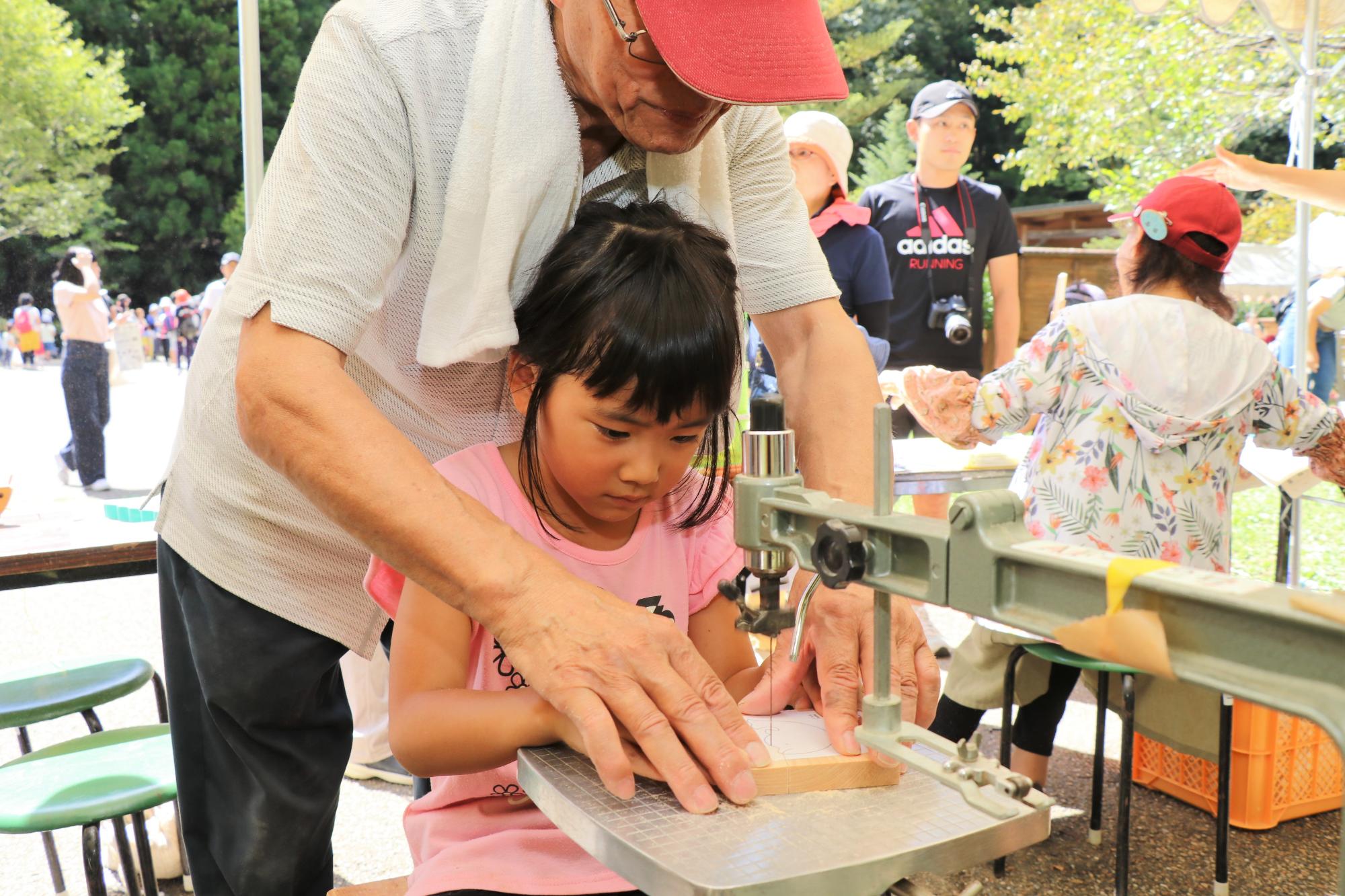 糸ノコで木工体験をする小学生と指導するスタッフの写真