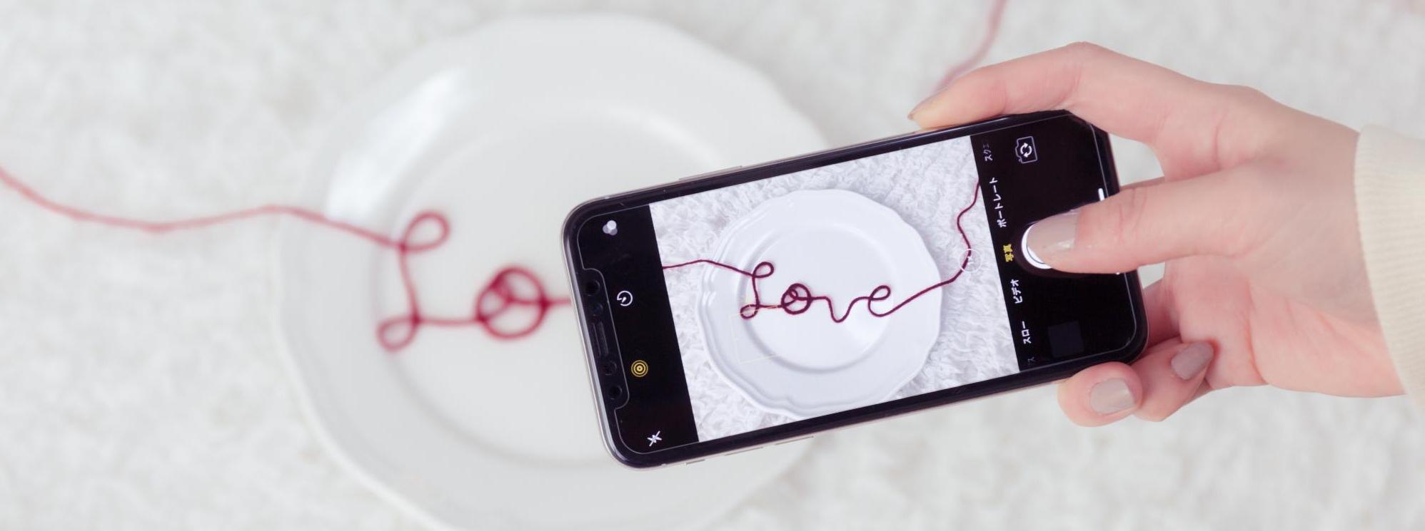 Loveと形どった赤い糸をスマートフォンで撮影している写真