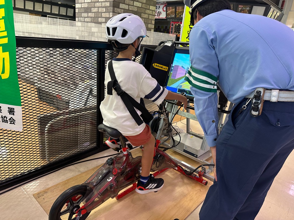 自転車シュミレーションを体験している子どもに警察官が説明をしている様子