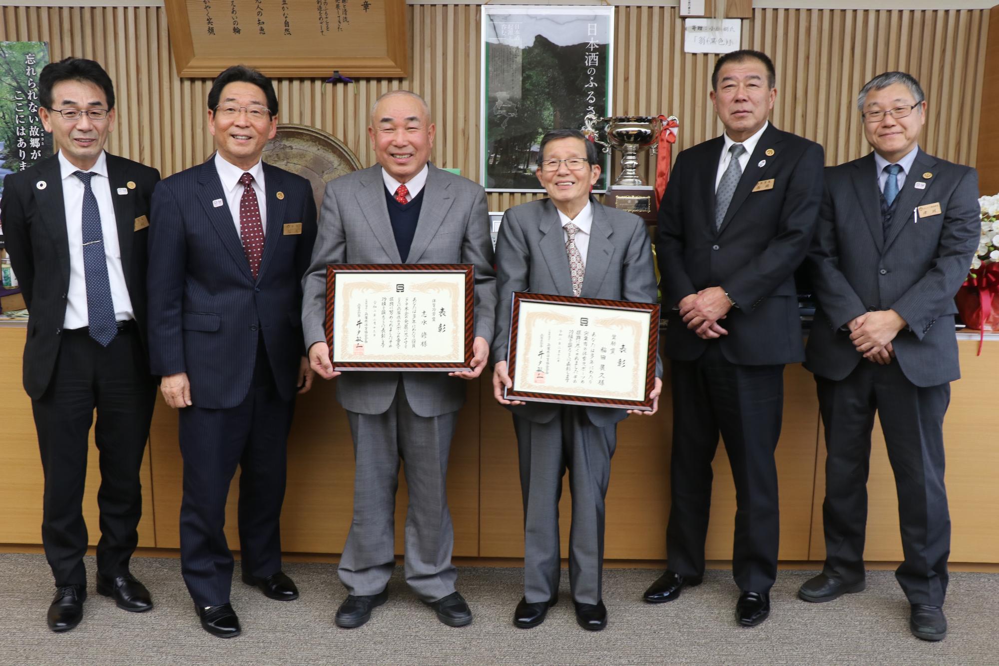 県体育功労賞と奨励賞を受賞した市体育協会の志水会長と稲田顧問が賞状をそれぞれ手に持ち、市長らと並んで笑っている写真