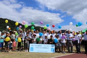 せせらぎ公園完成式典でカラフルな風船を手にしている関係者と子どもたちの記念写真