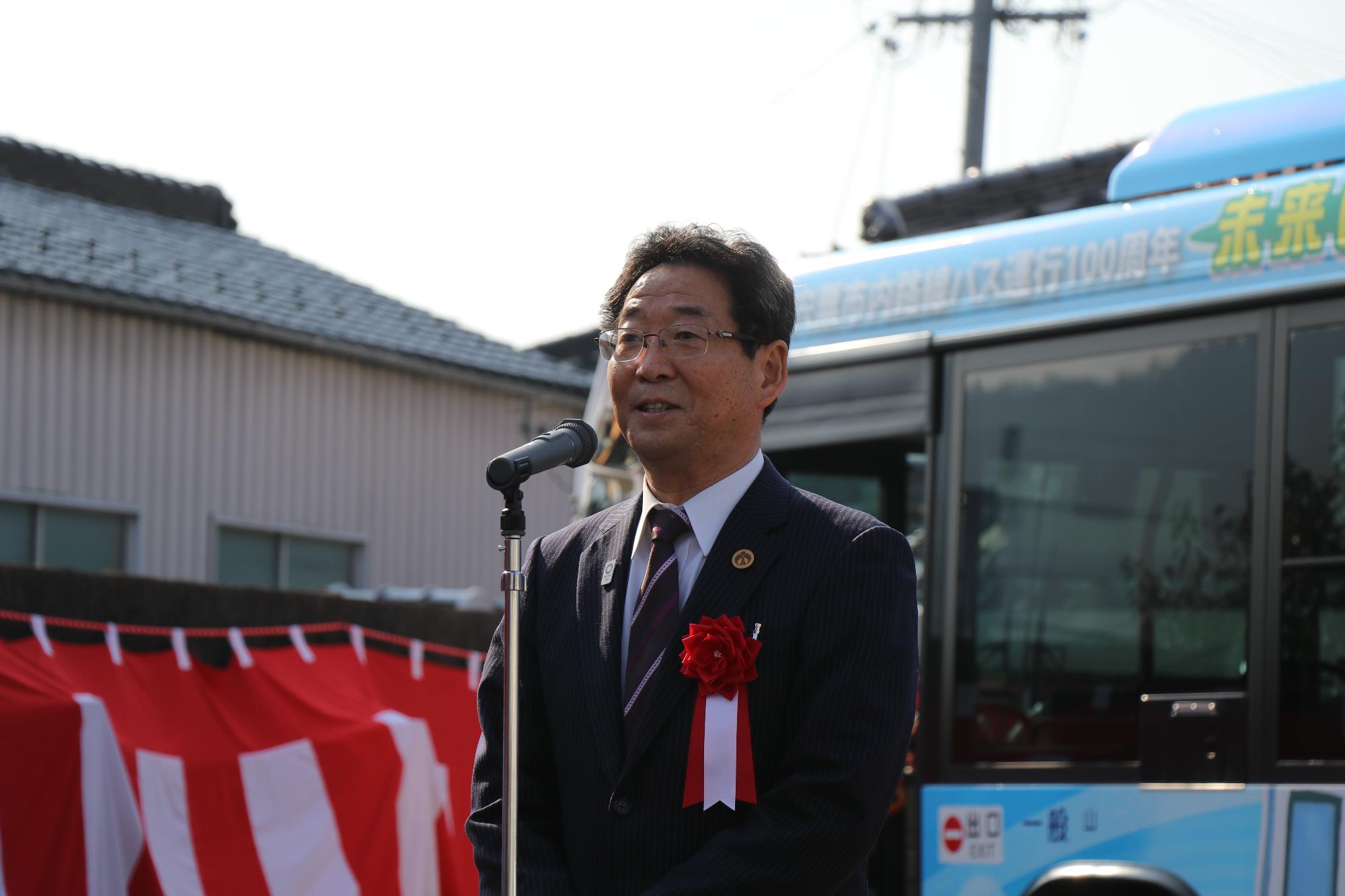 水色のバス運行100周年記念バスの前でスピーチを行う市長の写真