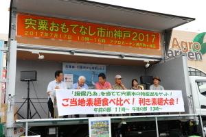 利き素麺大会に出場した5人の高齢の男女と市長がトラックの荷台のステージで利き素麺をしている写真