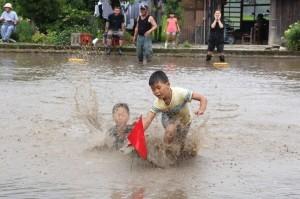 田んぼの真ん中に設置してある赤い旗を全力で走って取りに行っている2人の子ども達の写真