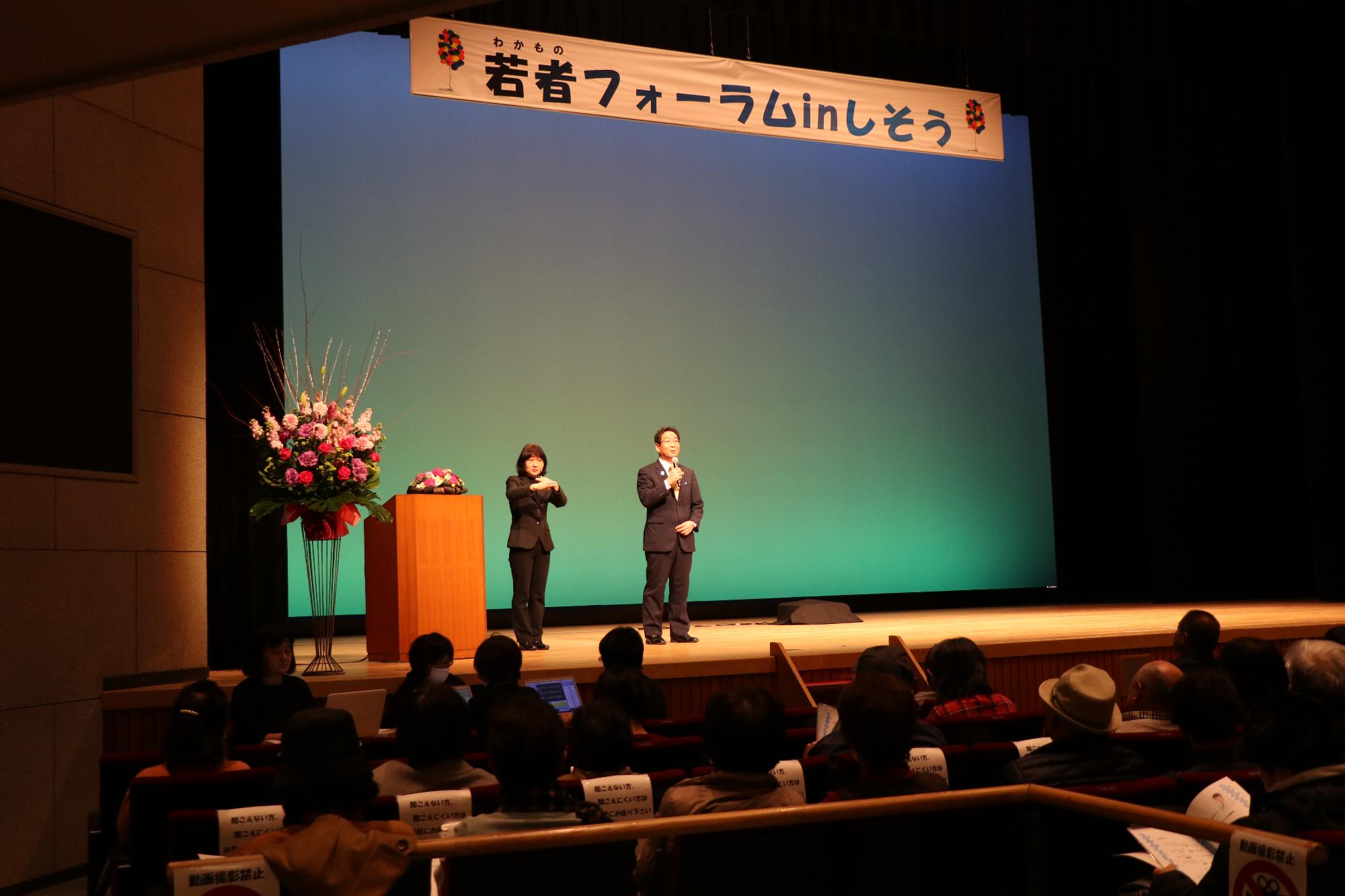 若者フォーラムのステージ上で通訳とともに挨拶をする市長の写真