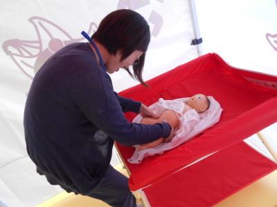 テント内で赤いおむつ交換台で赤ちゃんのおむつ交換をしている母親の写真
