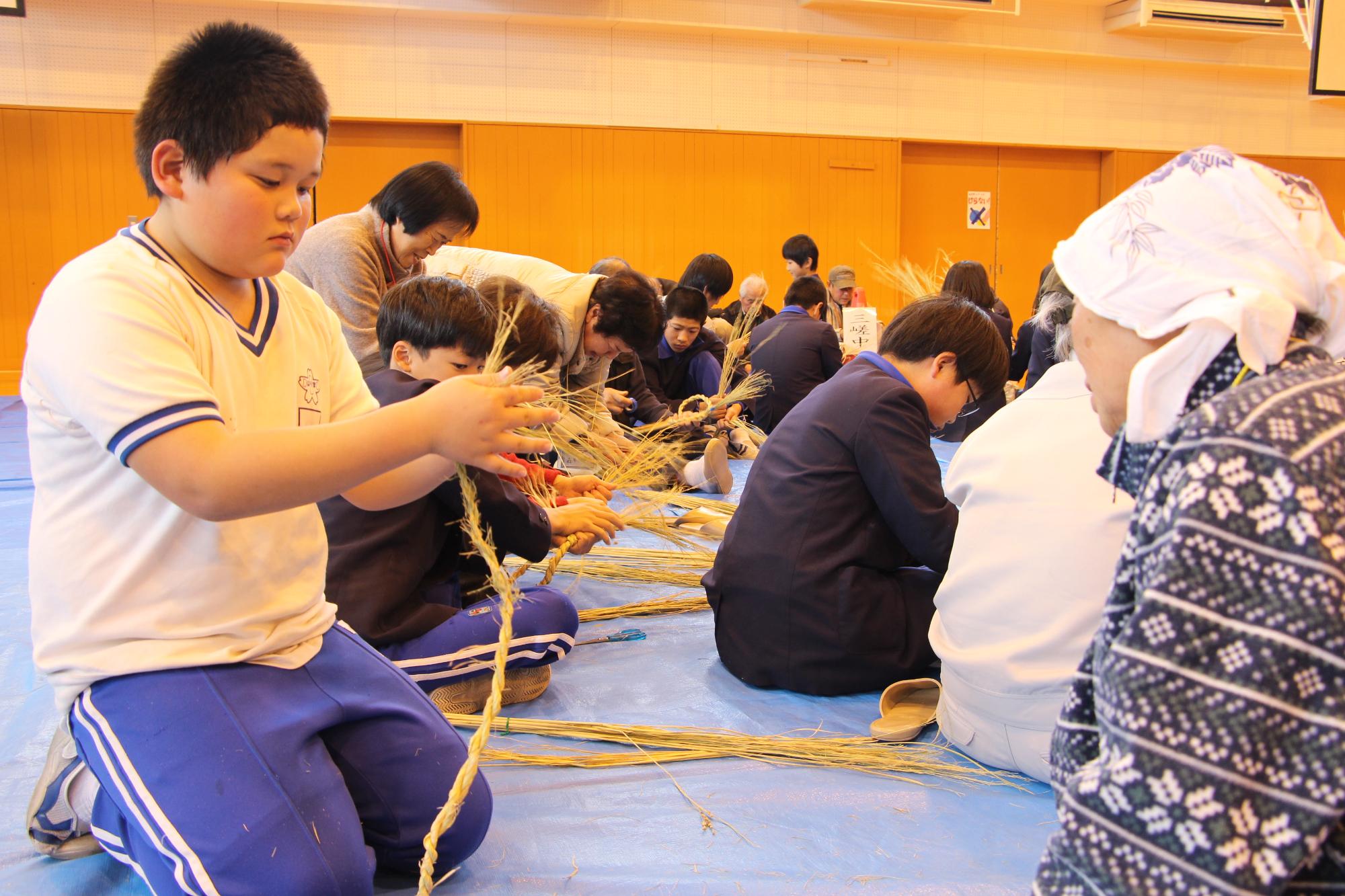 しめ縄作り体験で自分でわらを編んで縄を作っている小学生
