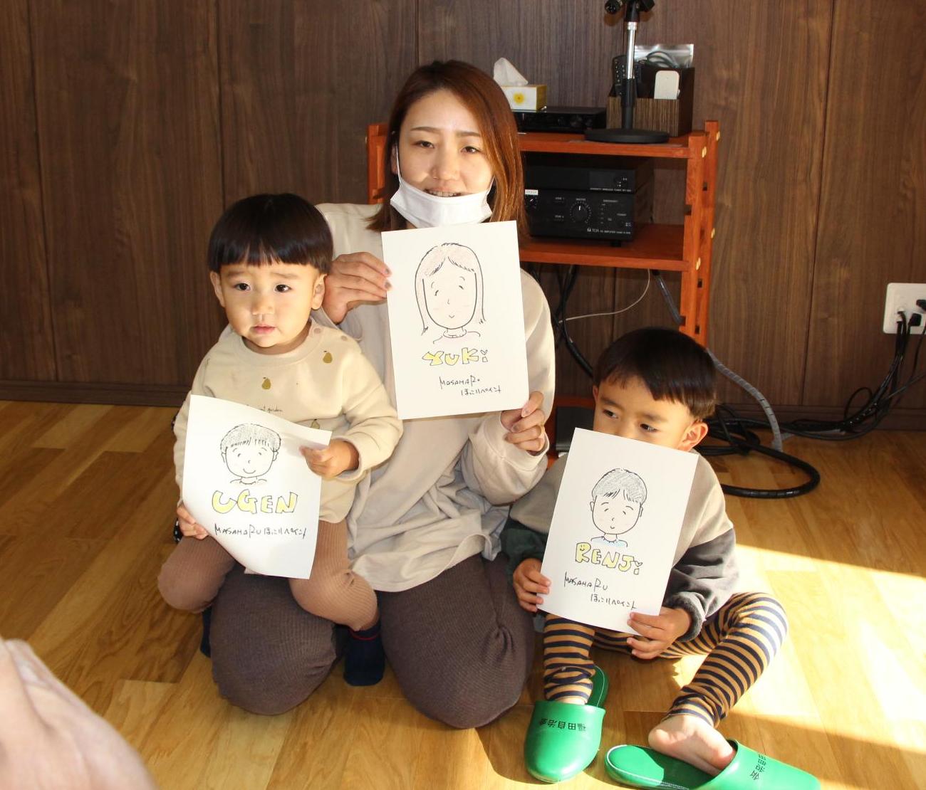 お母さんとお子さん二人が似顔絵と一緒に記念撮影しています。