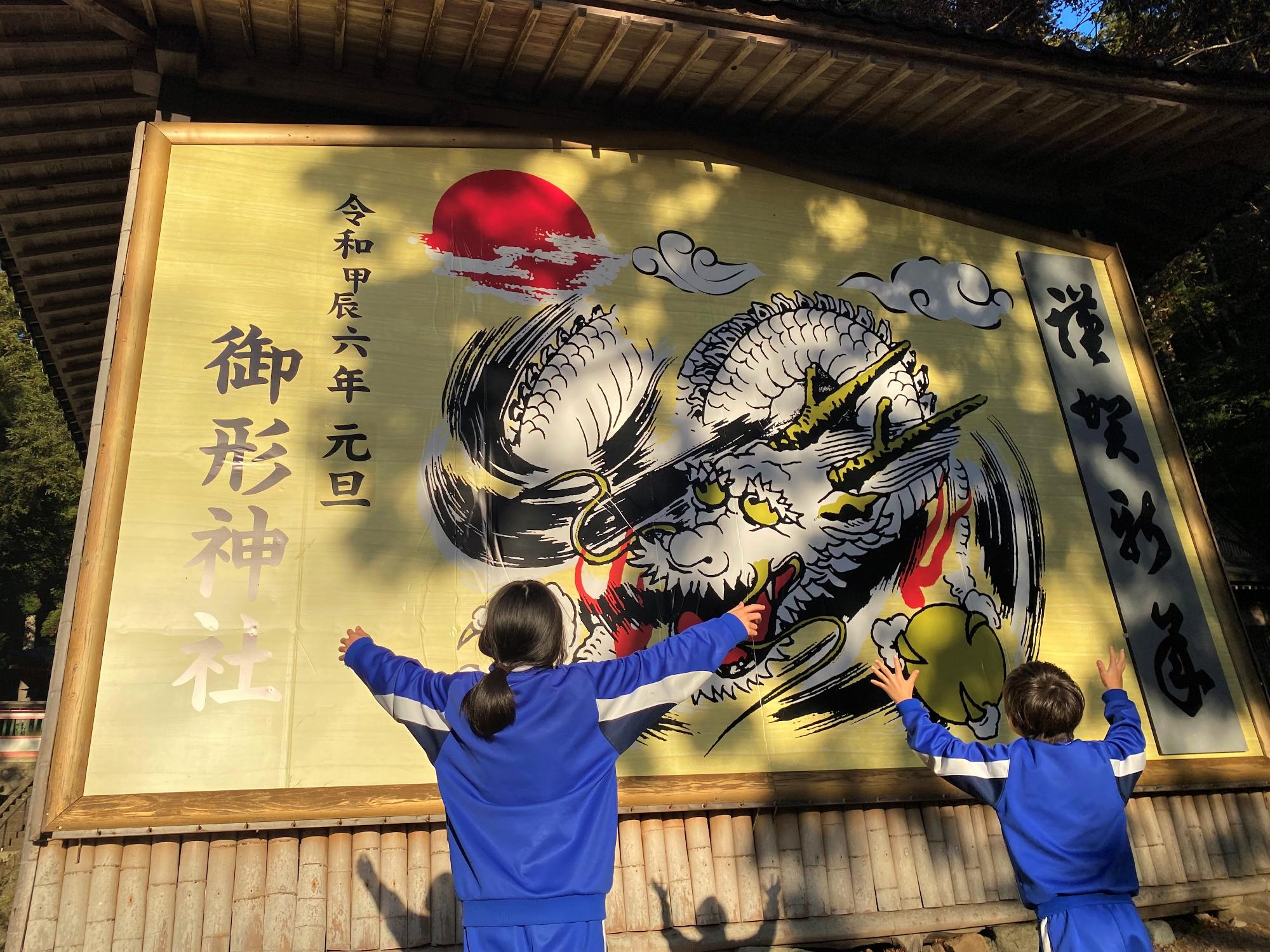 御形神社に掛けられた大絵馬の前で手を広げる子どもたち