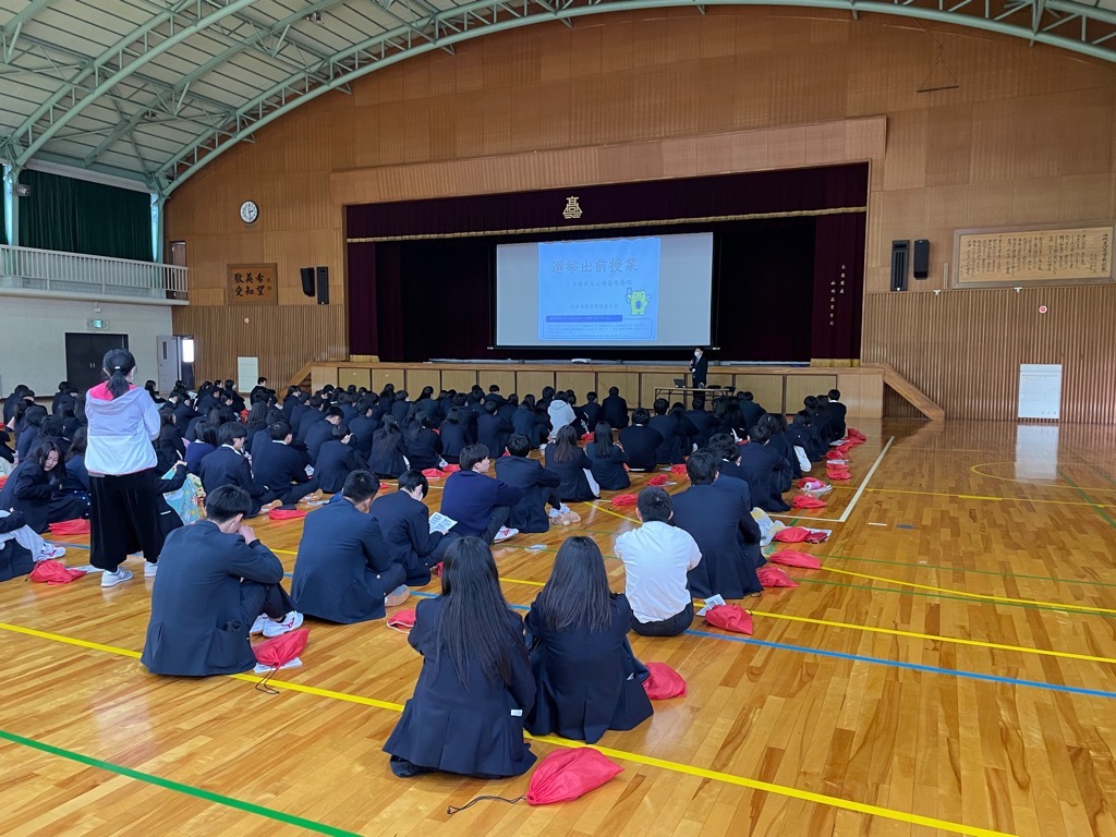 山崎高校の生徒が、体育館で選挙の出前授業を受けている写真