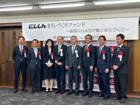 にししんまちづくりファンド設立の式典で、たつの市都市政策部の菅野部長、宍粟市の福元市長、姫路市の志々田副市長、 西兵庫信用金庫の桑垣理事長、MINTO機構の渡邉常務理事、国土交通省の太田室長、京都大学の山口准教授、 信金中央金庫神戸支店の草深支店長が胸に花をつけ横一列に並んで立っている写真