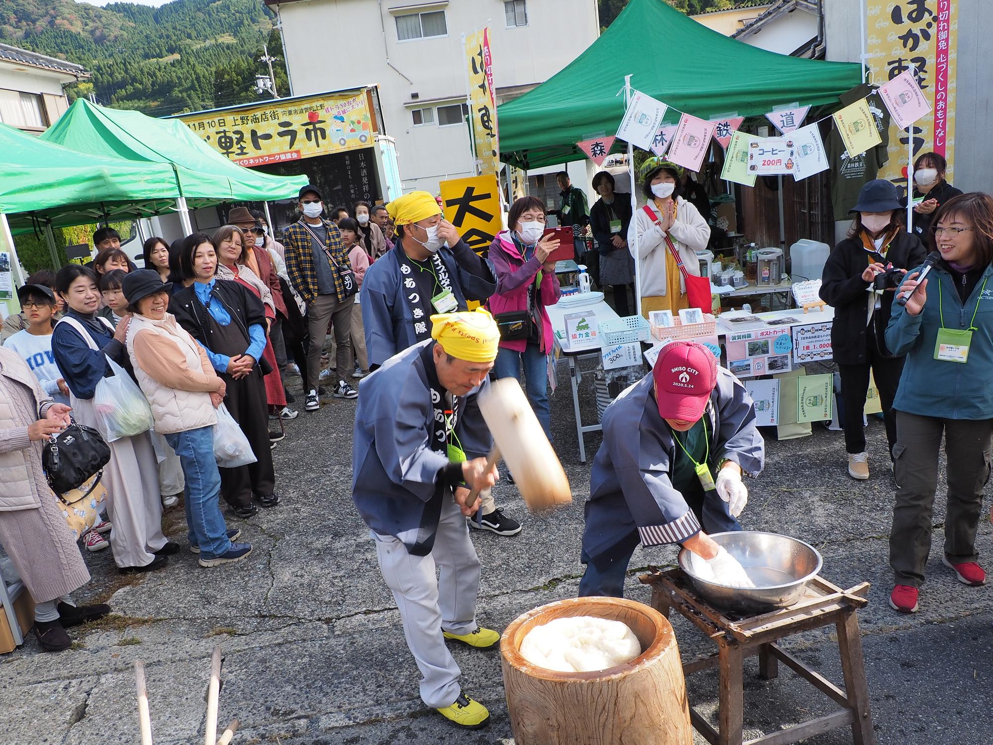 来場者が見守る中、メイプル餅つき隊のメンバーがイベント会場で餅つきを披露している写真
