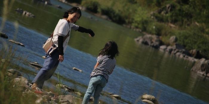 豊かな自然の中で川遊びをする母親と子供の写真
