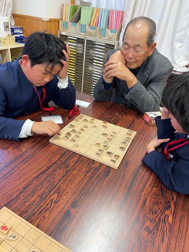 向かい合って将棋を指す小学生の一報が、最善手を打つために頭を悩ましている様子の写真