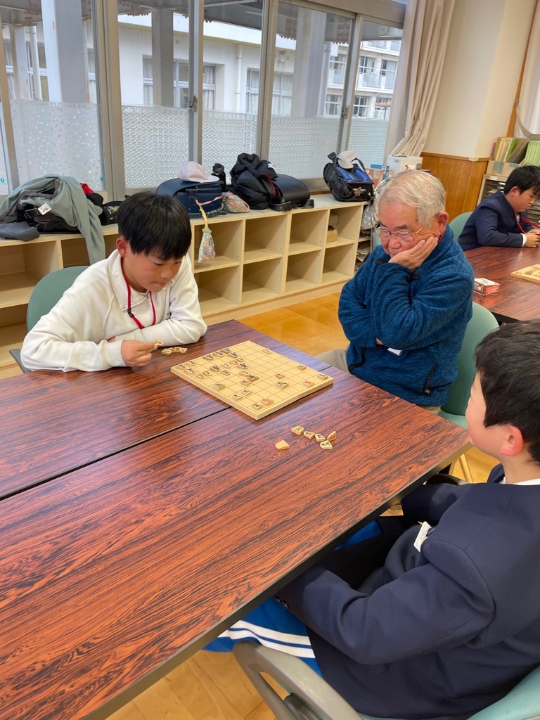 参加者が向かい合って将棋を指している横で、サポーターが神妙な様子で見守っている写真