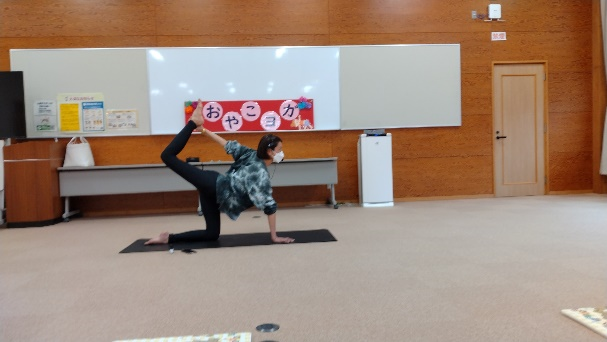 講師が手をついて座った状態から片足をあげ、手でその足をつかんだヨガのポーズを実演している写真