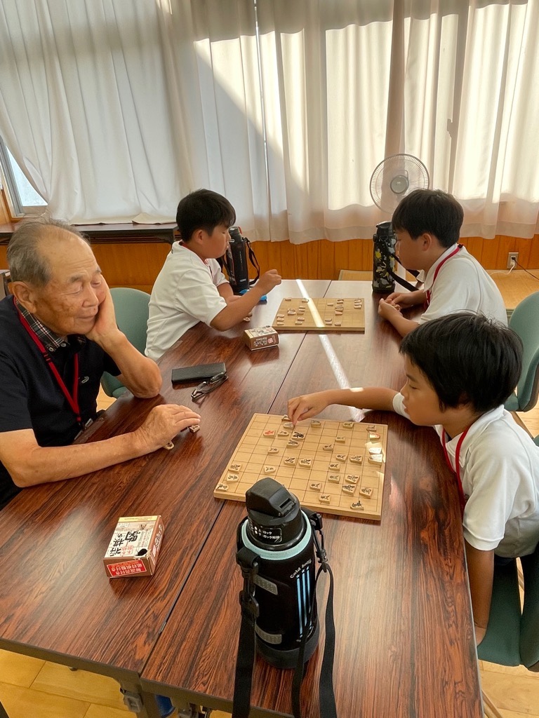 指導者と対局する参加者が将棋のコマを盤に置こうとしている写真