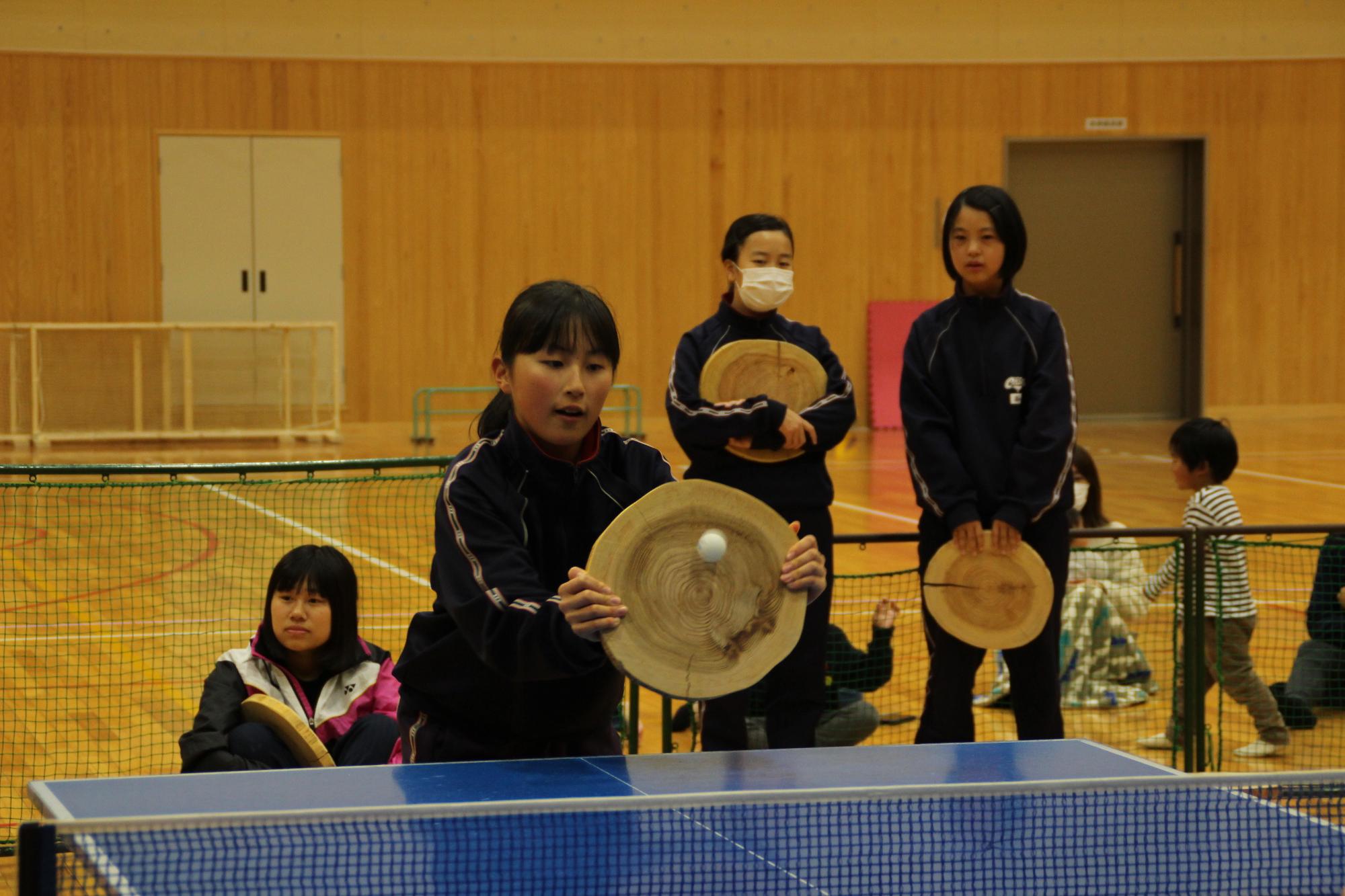 丸太ラケットで卓球の球を捉え返す女子中学生を正面側から撮った写真