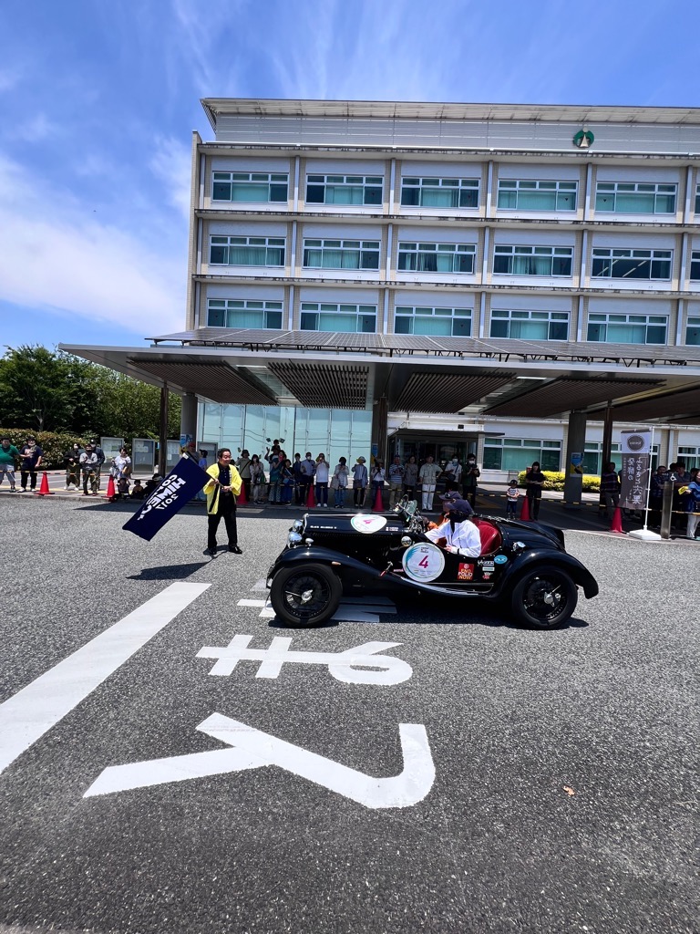 クラシックカーの前で旗をふる福元市長の写真