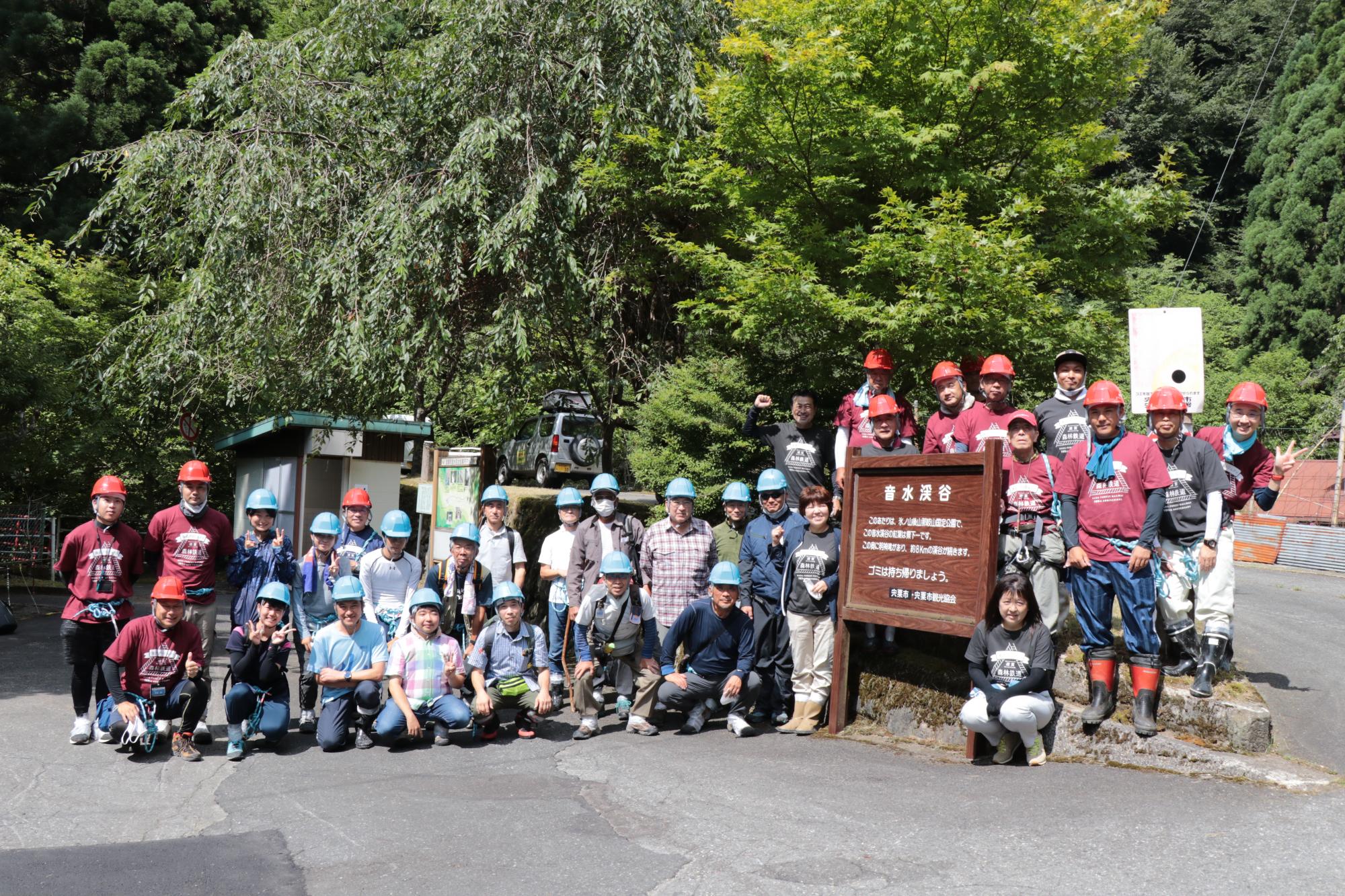 波賀林鉄再整備ツアーの参加者ら約30名が音水渓谷の入口に立つ看板付近に集まって並んでいる写真