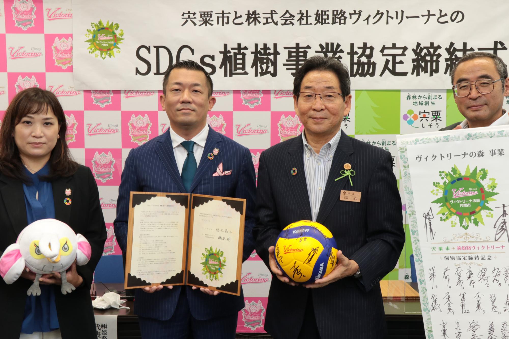 姫路ヴィクトリーナの竹下さんと橋本社長、福元市長と富田副市長が横一列に並び、協定書を手に微笑んでいる写真