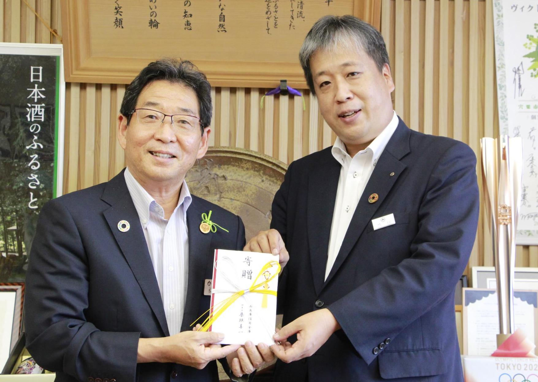 福元市長と西兵庫信用金庫の渋谷部長が横に並び、西兵庫信用金庫から市に寄付する34万円の目録にお互いの手を添えている写真