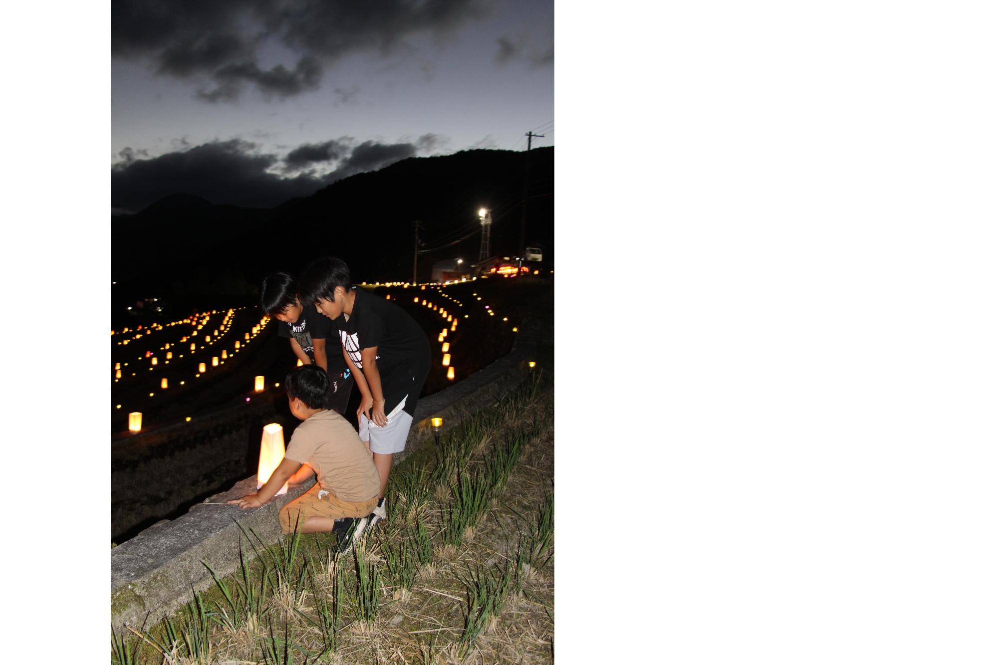 山田の棚田で灯籠の灯りをのぞき込む地元の子どもたちの画像