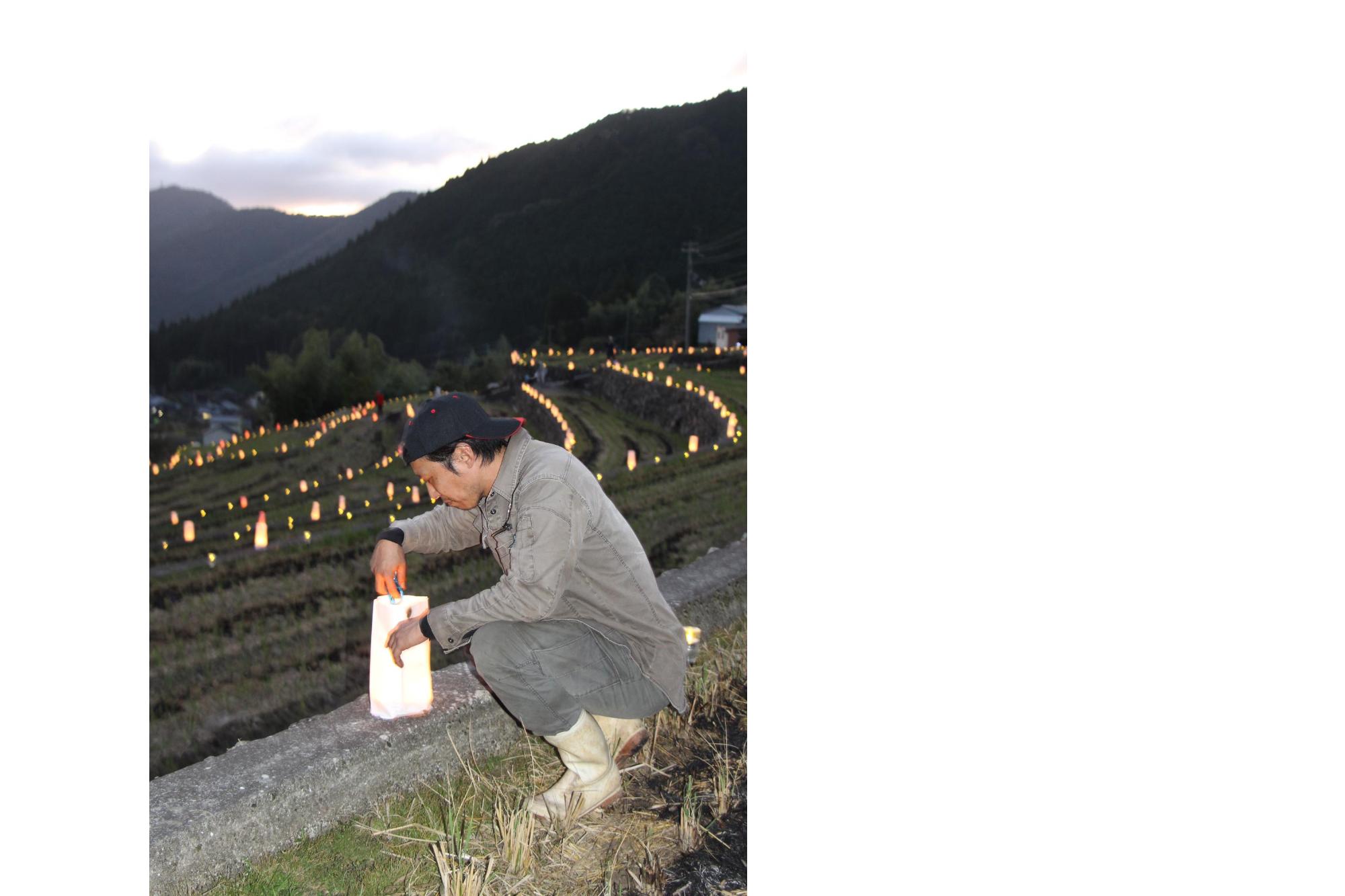 一宮町山田地区のイベント「棚田の灯り」で畦に置かれた灯籠に灯りをともす男性の画像